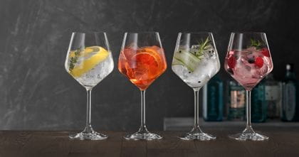 Four SPIEGELAU Gin and Tonic glasses on a wooden table, each of them filled with a different Gin cocktail.<br/>