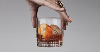 A lady's hand holding a Spiegelau Perfect Serve Collection S.O.F glass filled with an Old Fashioned cocktail.