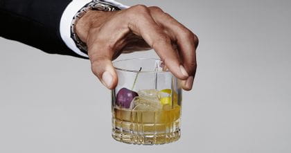 A man's hand holding the Spiegelau Perfect Serve Collection S.O.F glass filled with a Whisky Sour cocktail.