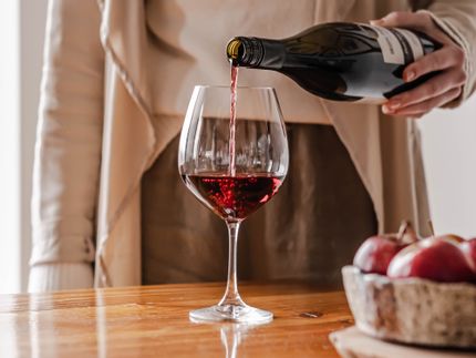 Lady pouring red wine into the SPIEGELAU Vino Grande Burgundy glass on a table top next to a bowl of apples.