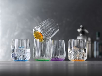 Las tazas SPIEGELAU Liefestyle en los colores océano, hoja, sol y lila están colocadas en fila. El vaso de color océano y sol está lleno de agua y cubitos de hielo.<br/>