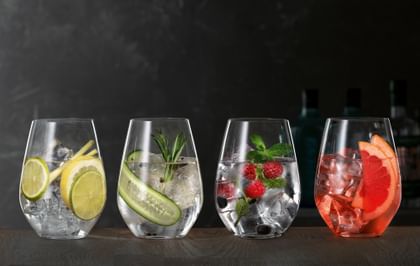 SPIEGELAU Gin and Tonic glasses on a wooden sideboard, each of thm filled with a different Gin Cocktail.<br/>
