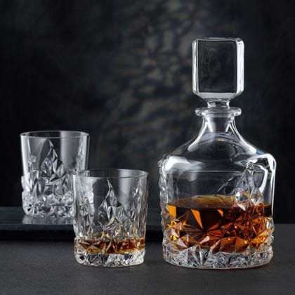 The NACHTMANN Sculpture Whiskey decanter besides the NACHTMANN Sculpture Whiskey tumbler, both of them filled with Whiskey. In the background an empty Sculpture tumbler on a serving tray.<br/>